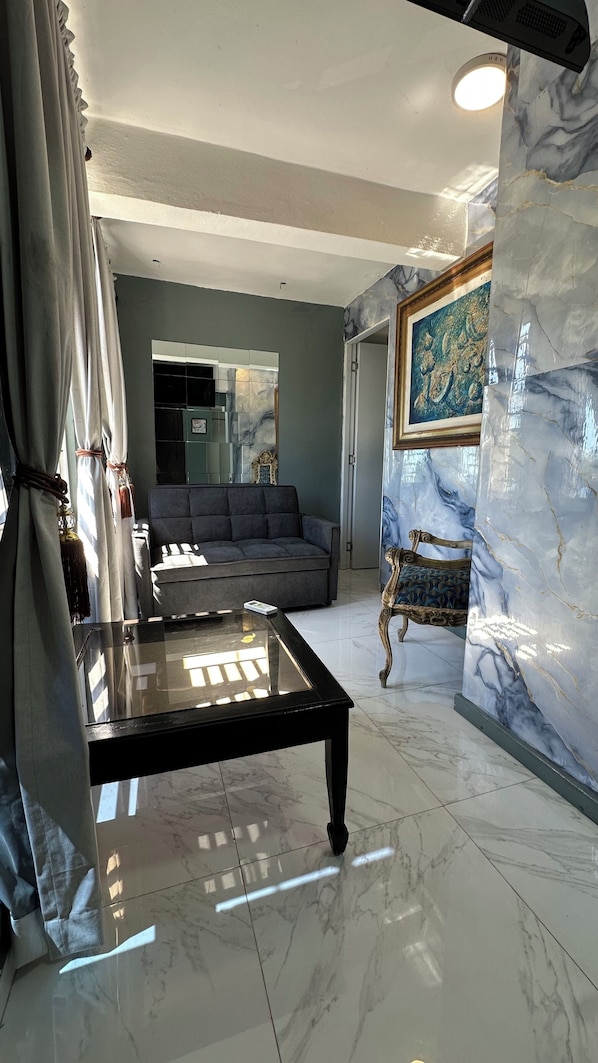 Un salon moderne avec un canapé, une table basse en verre et un mur décoratif en marbre.