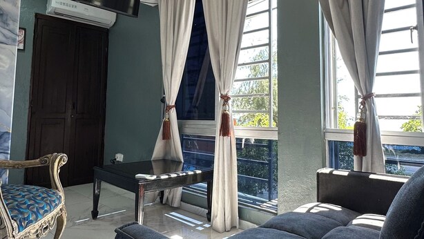 Una habitació amb un sofà, una cadira, una taula, un televisor i cortines.