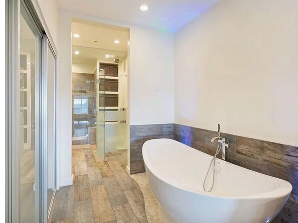 A modern bathroom with a freestanding bathtub, a glass shower enclosure, and a visible kitchen area.