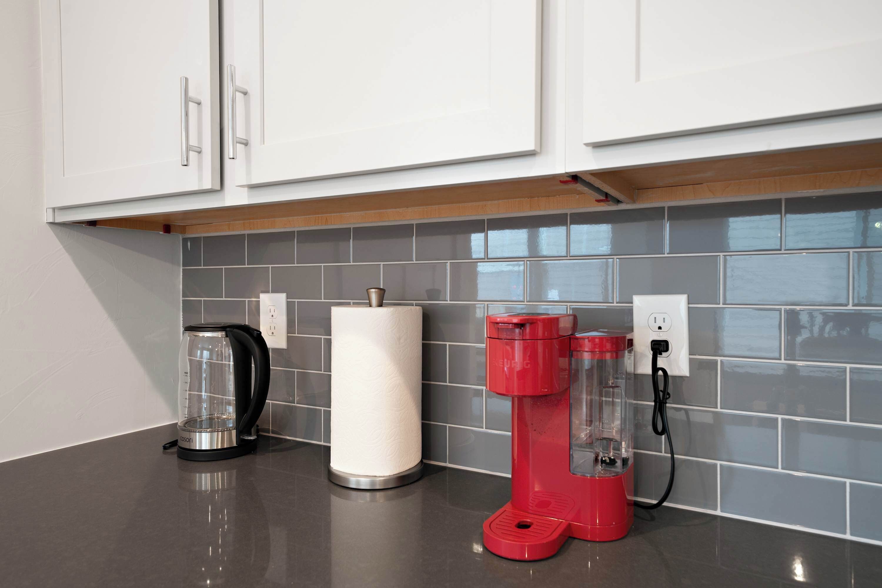 Une cuisine avec des meubles blancs, une machine à café et un appareil rouge placé sur un mur recouvert de carreaux.