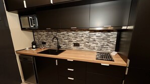 A modern kitchen with a black countertop, a sink, a microwave, and a tiled backsplash. - Le Jardin d'Eden JE112 - Suite Junior PMR Luxe - 2 people (AGDE)