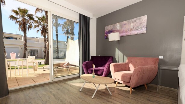 A modern room with a sliding glass door leading to a patio, a pink chair, a purple chair, and a wooden coffee table. - Le Jardin d'Eden JE112 - Suite Junior PMR Luxe - 2 people (AGDE)