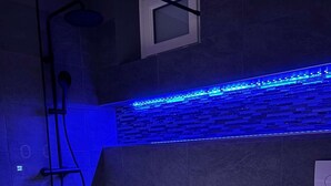 A modern bathroom with a glass shower enclosure, a toilet, and a blue LED light strip along the wall. - Le Jardin d'Eden JE112 - Suite Junior PMR Luxe - 2 people (AGDE)