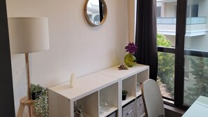 A modern room with a white console table, a mirror, a lamp, a potted plant, and a view of a building through a window. - Spacious studio in residence with swimming pool close to all amenities (Mougins)