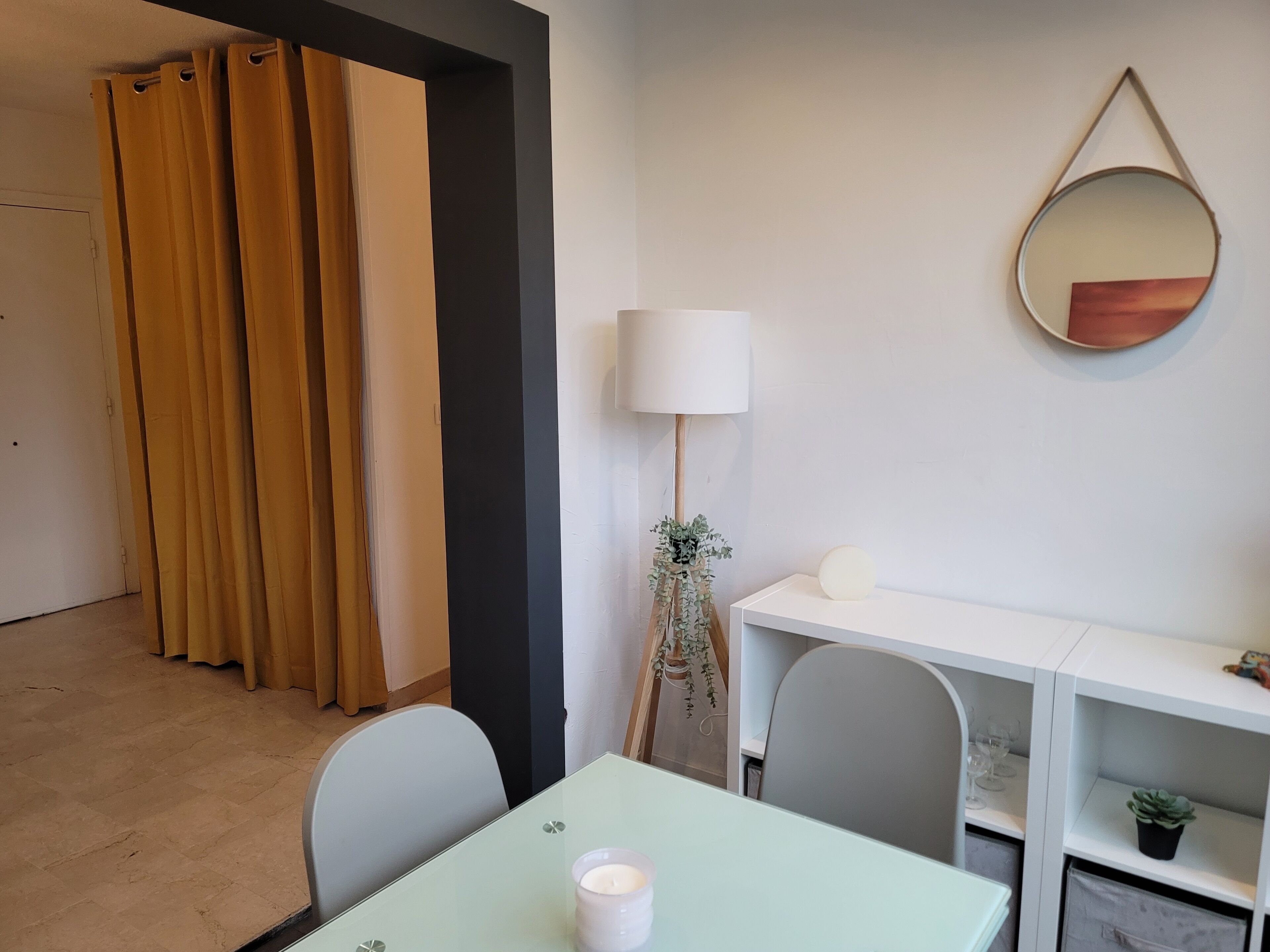 A room with a table, chairs, a lamp, a mirror, and a potted plant.
