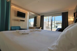 A hotel room with a large bed, a flat-screen TV mounted on the wall, a desk, and a view of the outdoors.