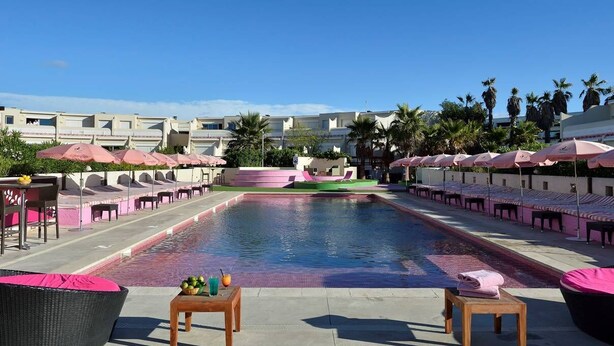 A pool area with lounge chairs and umbrellas, surrounded by buildings and palm trees. - Le Jardin d'Eden 104 - Suite Junior Luxe - 2 people (AGDE)