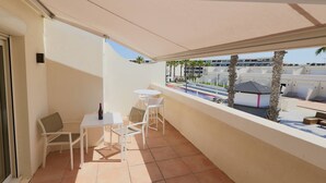 A balcony with white furniture, a bottle of wine, and a view of a pool and buildings. - Le Jardin d'Eden 211 - Suite Junior Premium - 2 people (AGDE)