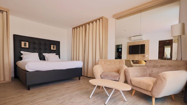Ein modernes Hotelzimmer mit einem großen Bett, zwei Sesseln, einem kleinen Tisch und einem Fernseher.