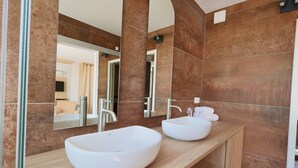 Ein modernes Badezimmer mit zwei weißen Aufsatzwaschbecken, einem großen Spiegel und braunen Fliesenwänden.