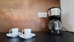 Eine Kaffeemaschine auf einer schwarzen Arbeitsplatte, dazu zwei weiße Tassen mit Untertassen.
