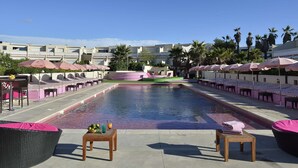 Una piscina con sillas de descanso y sombrillas, rodeada de edificios y palmeras.