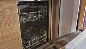 Un lavavajillas abierto en una cocina con un mueble de madera, un enchufe y una cafetera sobre la encimera.