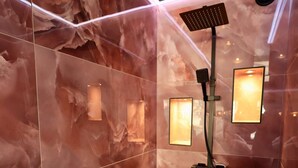 Un baño moderno con paredes de mármol, un cabezal de ducha de mano e iluminación empotrada.