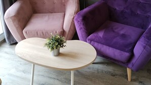 A room with a pink armchair, a purple sofa, a round wooden table with a plant, and a floor lamp against a dark wall. - Le Jardin d'Eden 113 - Suite Junior Premium - 2 people (AGDE)