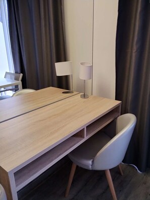 A modern room with a wooden desk, a white chair, a lamp, and a view of the outside through a window with curtains. - Le Jardin d'Eden 113 - Suite Junior Premium - 2 people (AGDE)