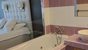 A modern bathroom with a large bathtub, a vanity with a sink, and a mirror above the sink. - Le Jardin d'Eden 113 - Suite Junior Premium - 2 people (AGDE)