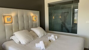 A modern hotel room with a large bed, two bedside lamps, a large window, and a view of the outside. - Le Jardin d'Eden JE135 - Suite Junior Luxe with garage - 2 people (AGDE)