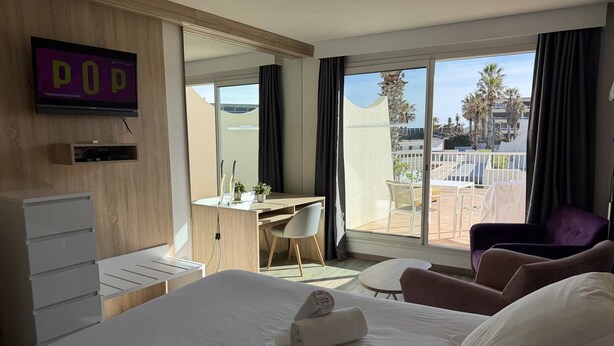 A hotel room with a bed, a desk, a chair, a TV, and a balcony with a view. - Le Jardin d'Eden JE135 - Suite Junior Luxe with garage - 2 people (AGDE)