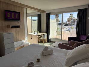 Une chambre d’hôtel avec un lit, un bureau, une chaise, une télévision et un balcon offrant une vue.