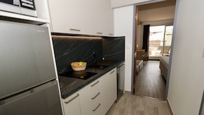 A compact kitchen with a built-in refrigerator, a black marble countertop, and a basket with fruit. - Le Jardin d'Eden JE135 - Suite Junior Luxe with garage - 2 people (AGDE)