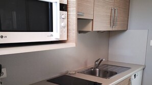 Een kleine keuken met een magnetron, spoelbak, fornuis en houten kastjes.
