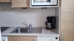 Una cocina equipada con microondas, cafetera, lavaplatos e instalación de lavamanos.