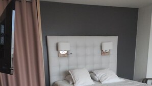 Una habitación de hotel con una cama, un escritorio con lámpara y un televisor montado en la pared.