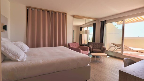 Habitación de hotel con una cama grande, dos sillones, una mesita y un balcón con tumbonas.