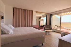 Ein Hotelzimmer mit einem großen Bett, zwei Sesseln, einem kleinen Tisch und einem Balkon mit Liegestühlen.