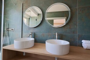 Ein Badezimmer mit zwei runden weißen Waschbecken, einem Spiegel und einer Dusche.