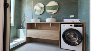 Un baño moderno con cabina de ducha de vidrio, un tocador de madera con lavabo y espejo, y una lavadora de carga frontal.