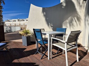 An outdoor patio with a white table and chairs, a potted plant, and a view of a building in the background. - Le Jardin d'Eden - Suite Junior Luxe 139 with large terrace - 2 people (AGDE)
