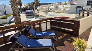 Un espace de détente aménagé sur le toit, avec des chaises longues, une piscine et un palmier.