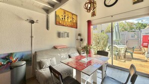 A cozy living room with a sofa, a dining table, and chairs. There is a painting on the wall, a clock, and a hanging light fixture. - CAP D'AGDE - MONT ST MARTIN // Réf 0314 (CAP D'AGDE)