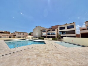 A swimming pool area with multiple pools and a building complex in the background. - CAP D'AGDE - MONT ST MARTIN // Réf 0314 (CAP D'AGDE)