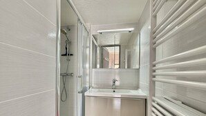 A bathroom with a glass shower enclosure, a sink with a mirror above it, and a towel rack with a pink towel. - CAP D'AGDE - Richelieu // Réf 0309 (CAP D'AGDE)