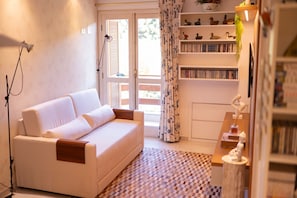 Un salon confortable avec un canapé, une bibliothèque et une fenêtre avec des rideaux.