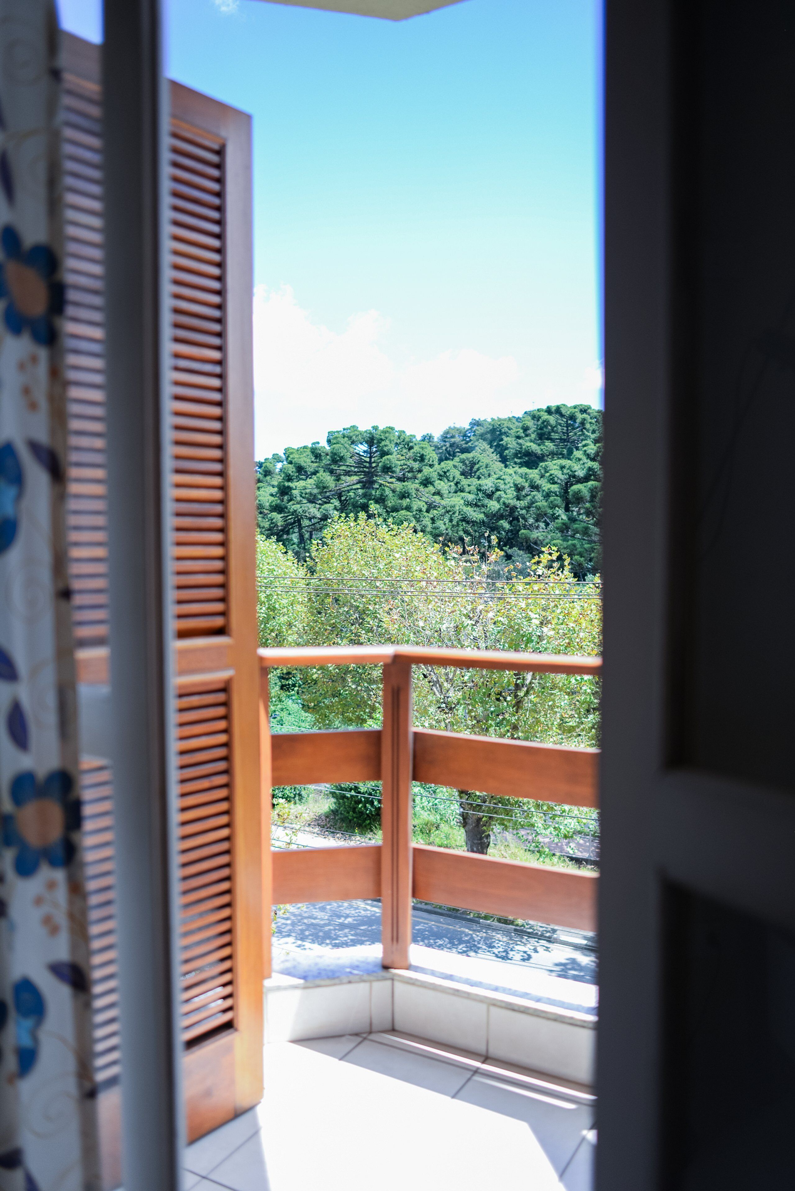 A view from a balcony with wooden railings and a tiled floor, overlooking a forested area.