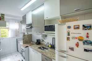 A modern kitchen with a microwave, refrigerator, and sink. There are decorative magnets on the fridge and a window with curtains.