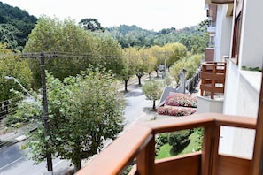 Un immeuble résidentiel doté d’un balcon donnant sur une rue bordée d’arbres et sur un jardin.