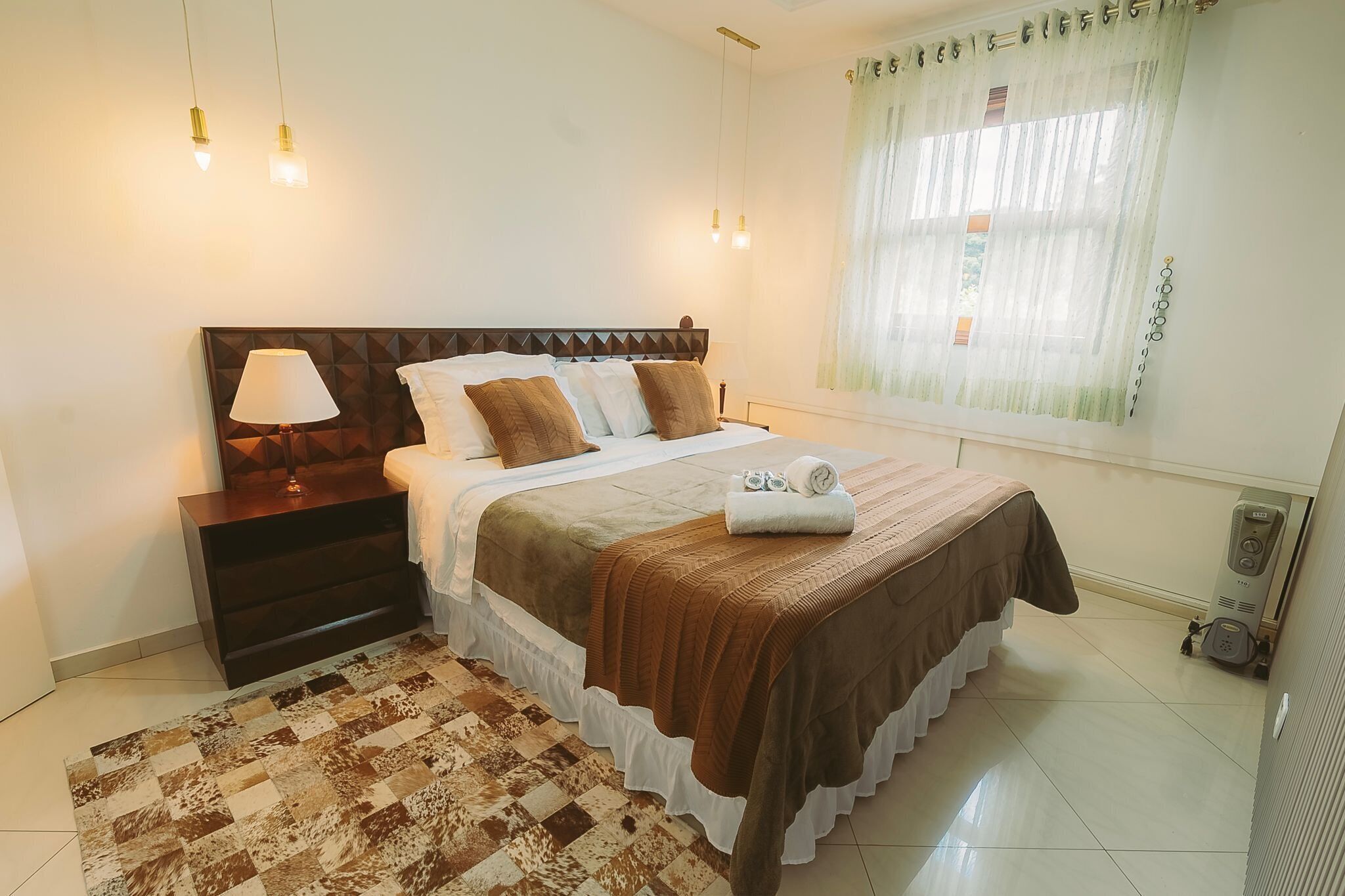 A neatly arranged bedroom with a bed, bedside table, lamp, and a heater.