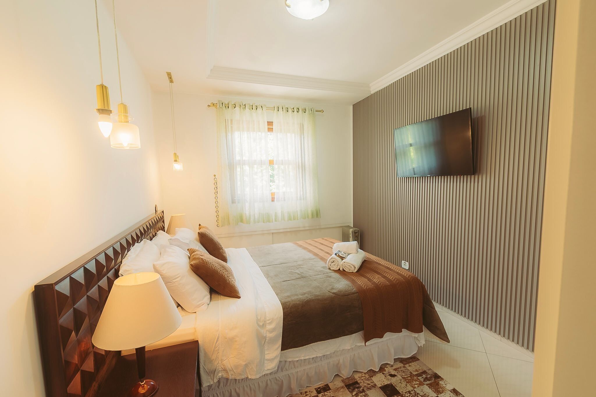 A hotel room with a bed, a TV mounted on the wall, and a window with curtains.