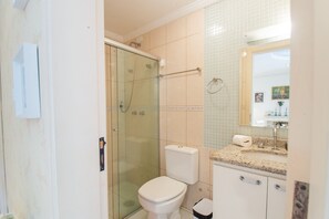 A bathroom with a glass-enclosed shower, a toilet, and a sink with a mirror above it. - Apto no Coração do Capivari e Perto de Tudo (Campos do Jordão)