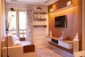 A modern living room with a sofa, a TV mounted on a wooden wall, and a bookshelf with decorative items.