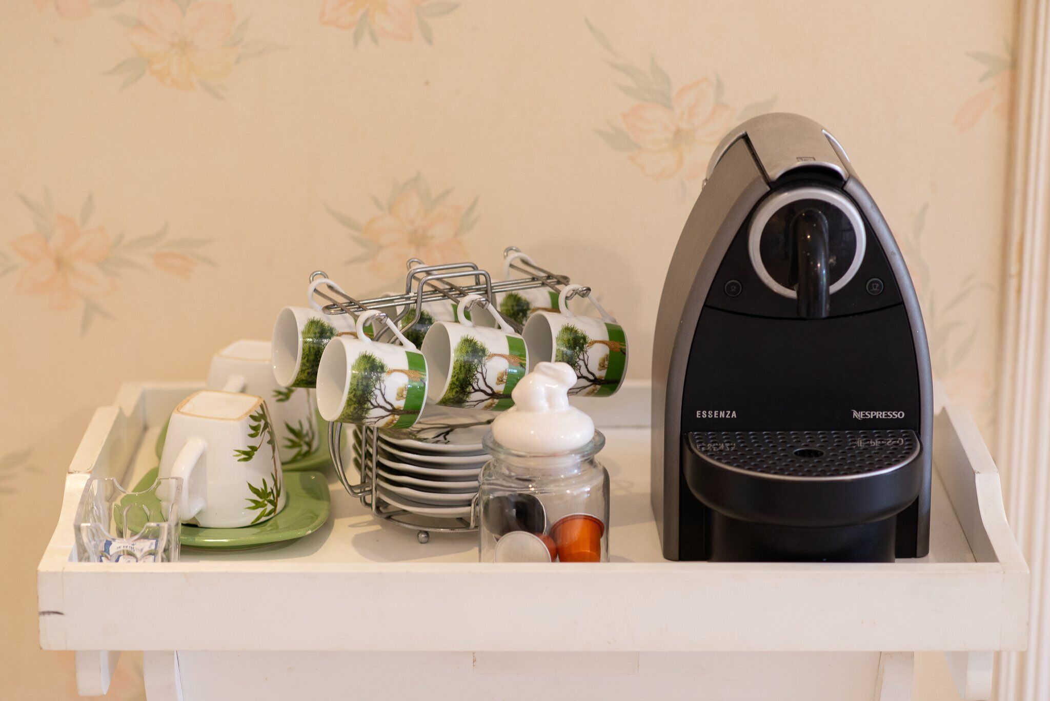Eine Küchenzeile mit einer Kaffeemaschine, einem Stapel Teller und einer Ablage mit Tassen und einem kleinen Glas.