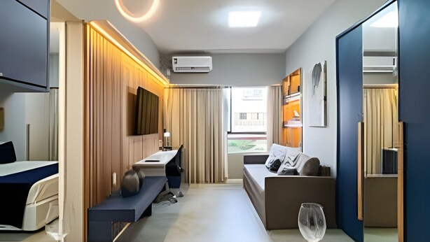 A modern hotel room with a dining area, a sofa, a TV, and an air conditioning unit. - Flat na melhor localização de Boa Viagem (Recife)