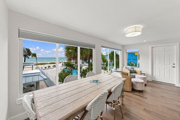 A spacious room with a large dining table, wicker chairs, and a view of a beach and pool. - BG Beach Club 3E | 3BR/2BA Boca Grande Condo (Boca Grande)