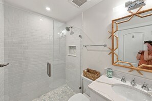 A modern bathroom with white subway tiles, a glass shower enclosure, a wooden-framed mirror, and a marble sink. - BG Beach Club 3E | 3BR/2BA Boca Grande Condo (Boca Grande)