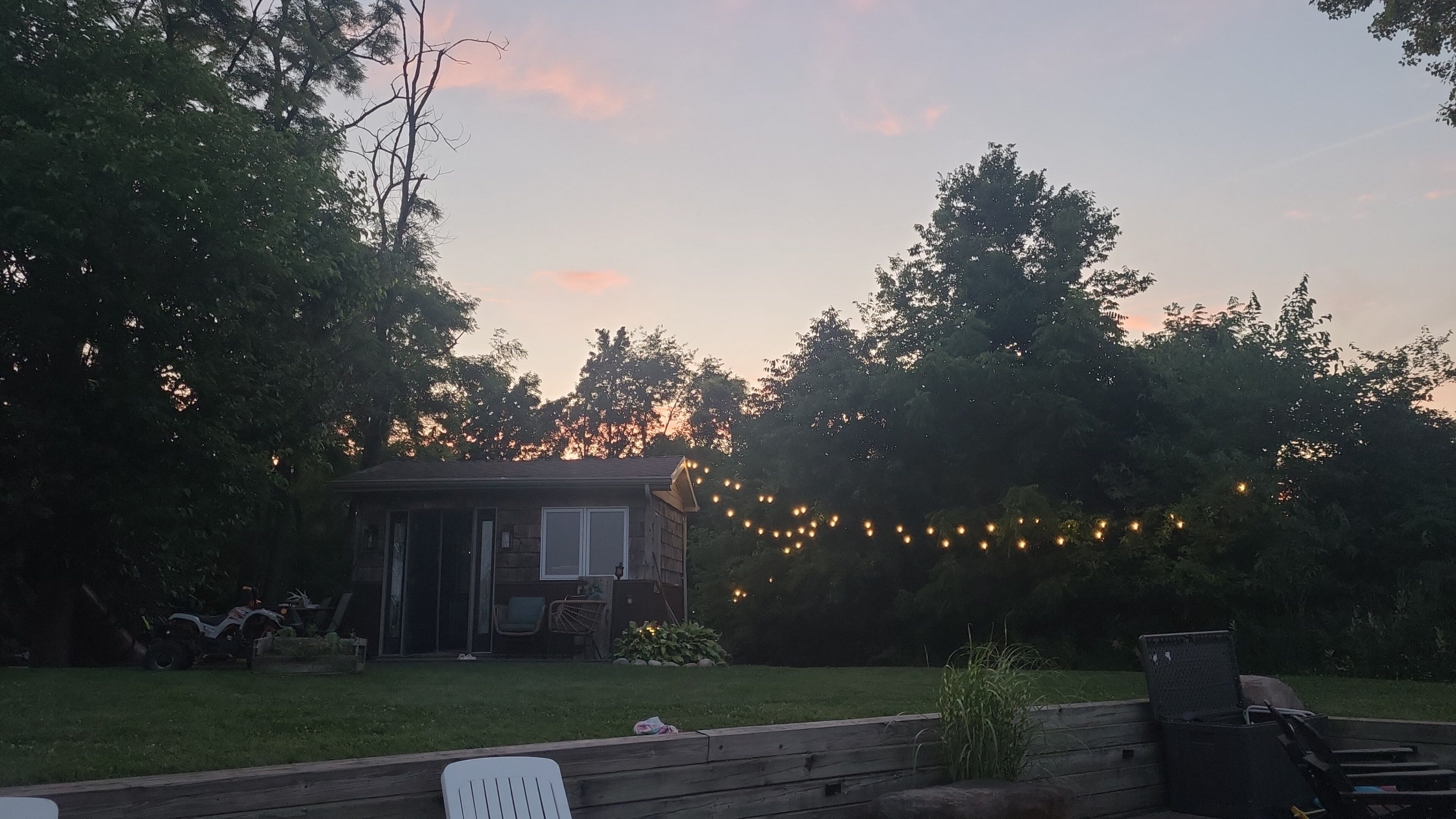 Une cabane en bois dotée d’un patio, entourée d’arbres et illuminée de guirlandes lumineuses.